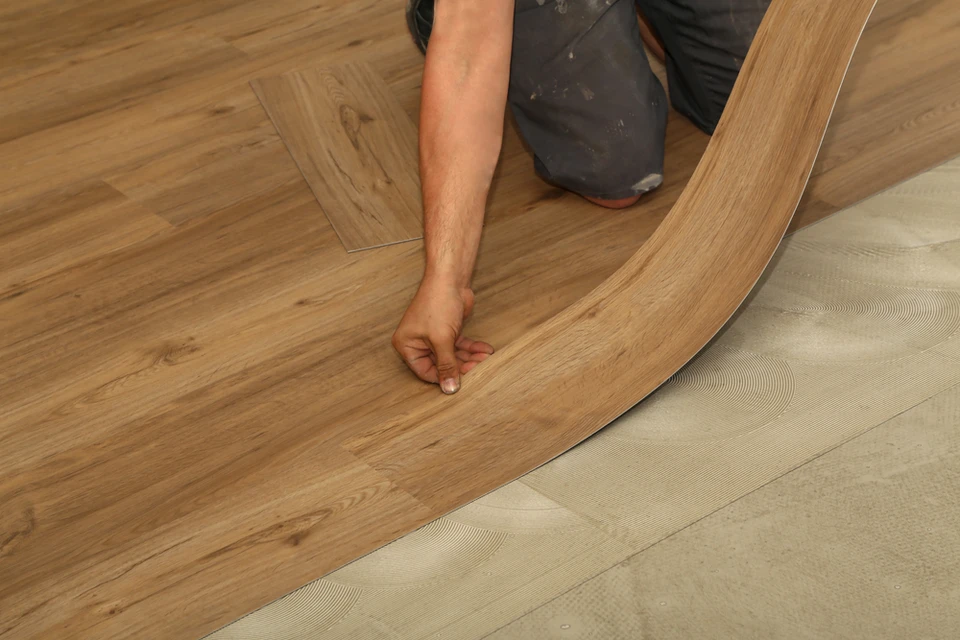 Intérieur résidentiel avec artisan à genoux installant un parquet contrecollé aspect chêne naturel sur sous-couche isolante